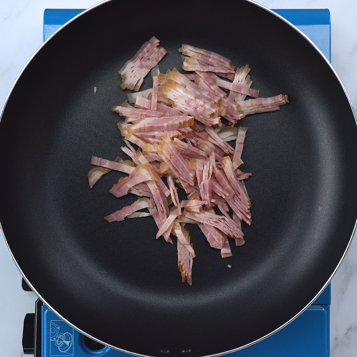 Bacon dourando em frigideira até ficar crocante para carbonara.
