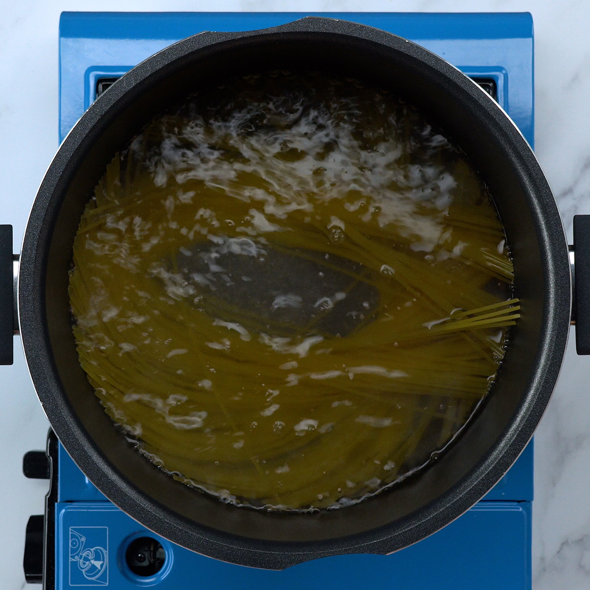 Espaguete cozinhando em panela grande com água fervente e sal.