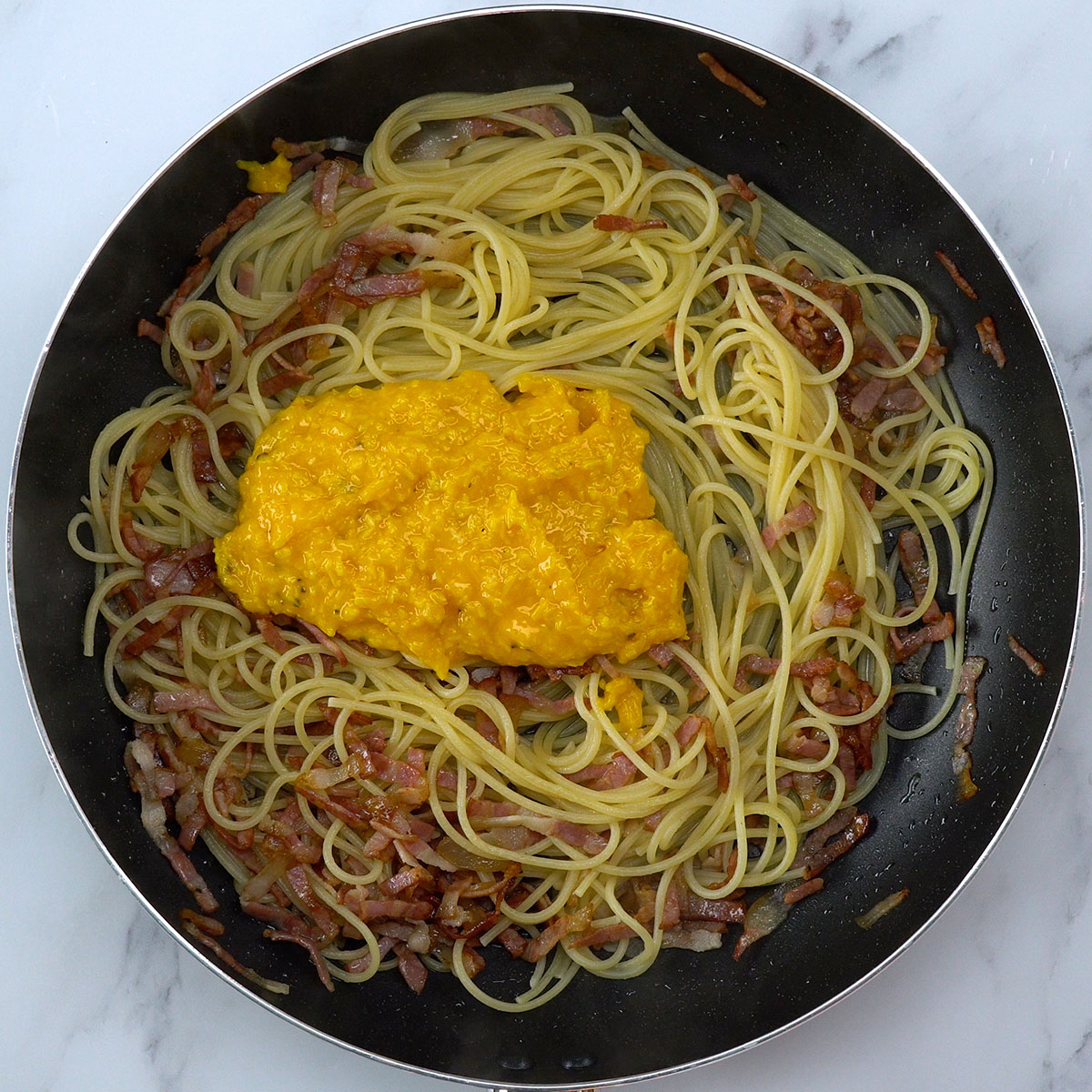 Molho carbonara cremoso sendo preparado com gemas, parmesão e espaguete quente.