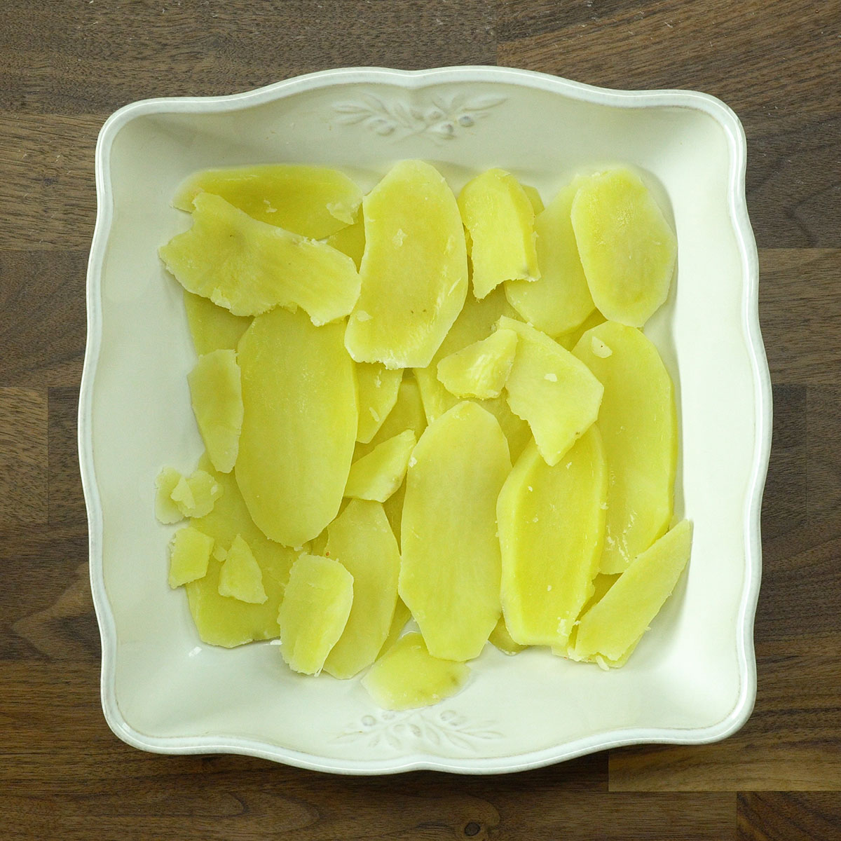 Camada de batatas cozidas organizada no refratário para peixe ao forno.