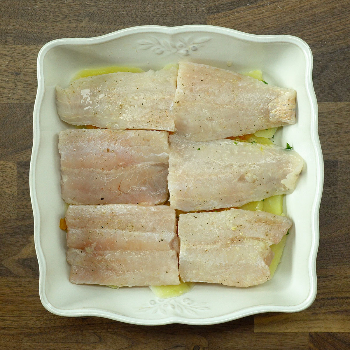 Filetes de pescada organizados sobre molho e batatas no refratário.