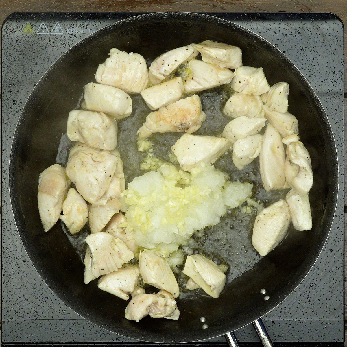 Frango sendo refogado com cebola e alho picados até ficarem macios.