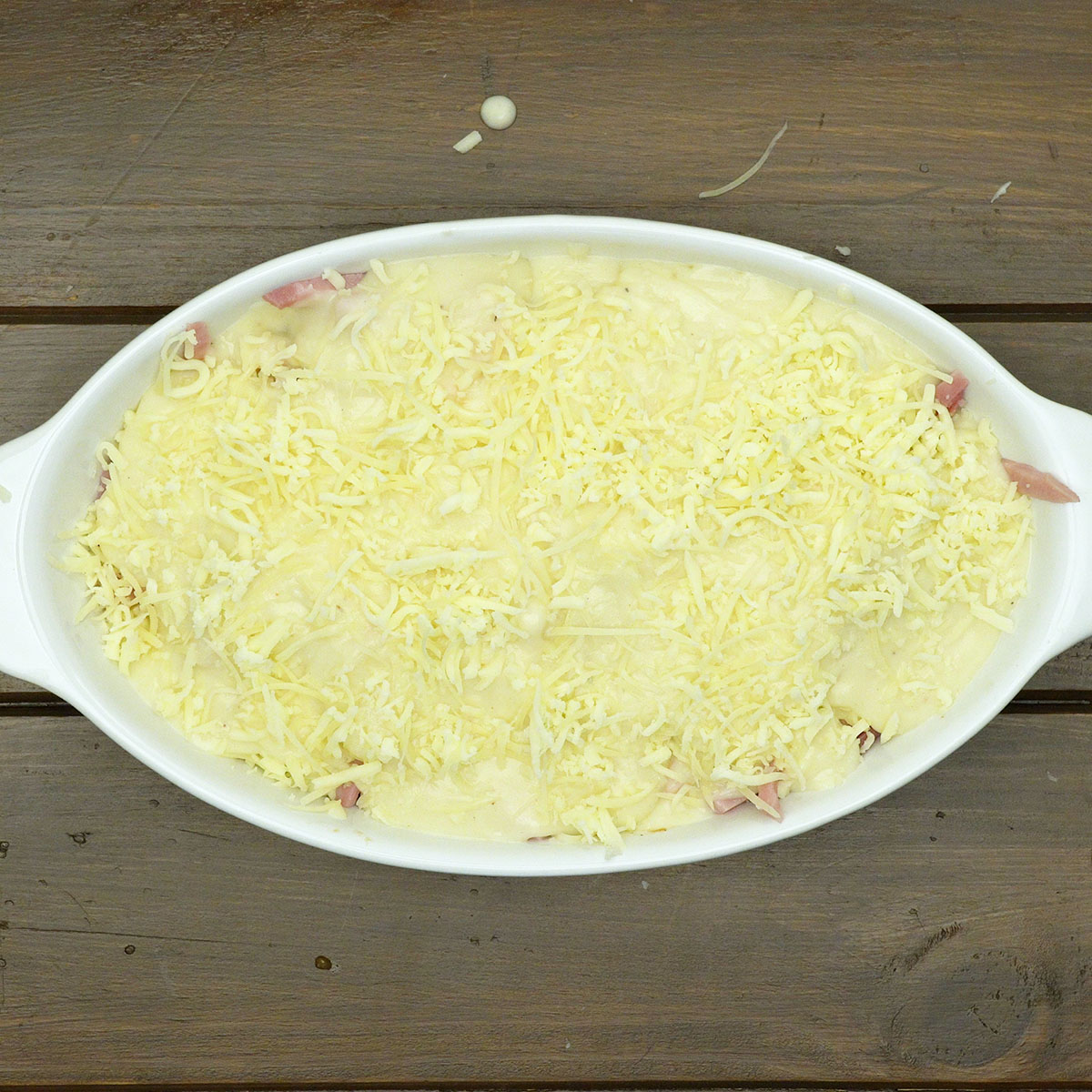 Frango ao molho branco coberto com queijo antes de gratinar no forno.