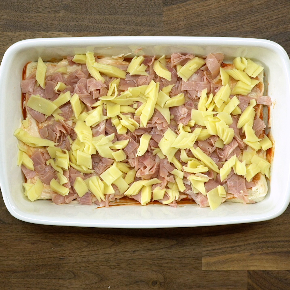 Presunto e muçarela sendo adicionados ao lachão de pizza caseiro.