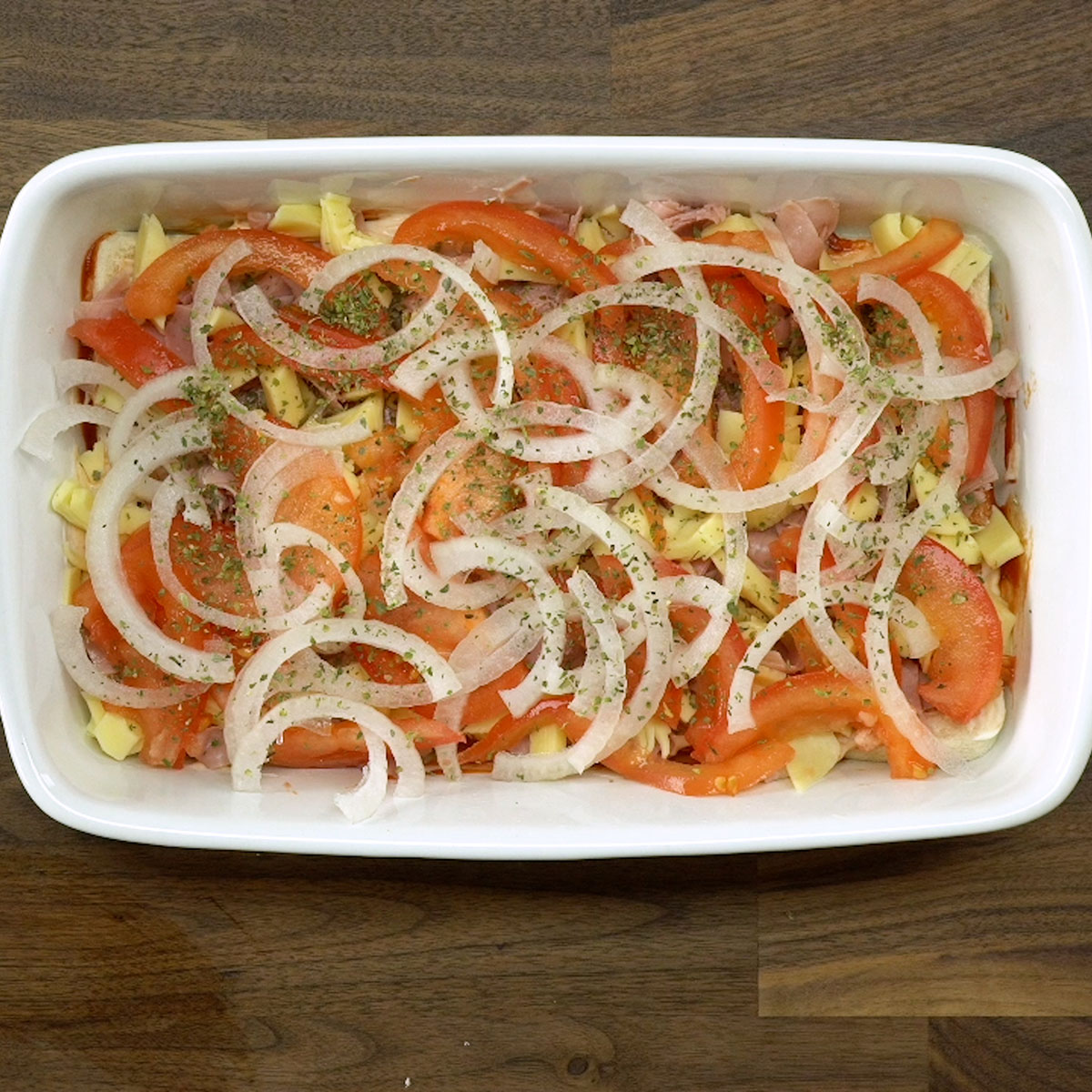 Tomate, cebola e orégano distribuídos sobre o lachão de pizza.
