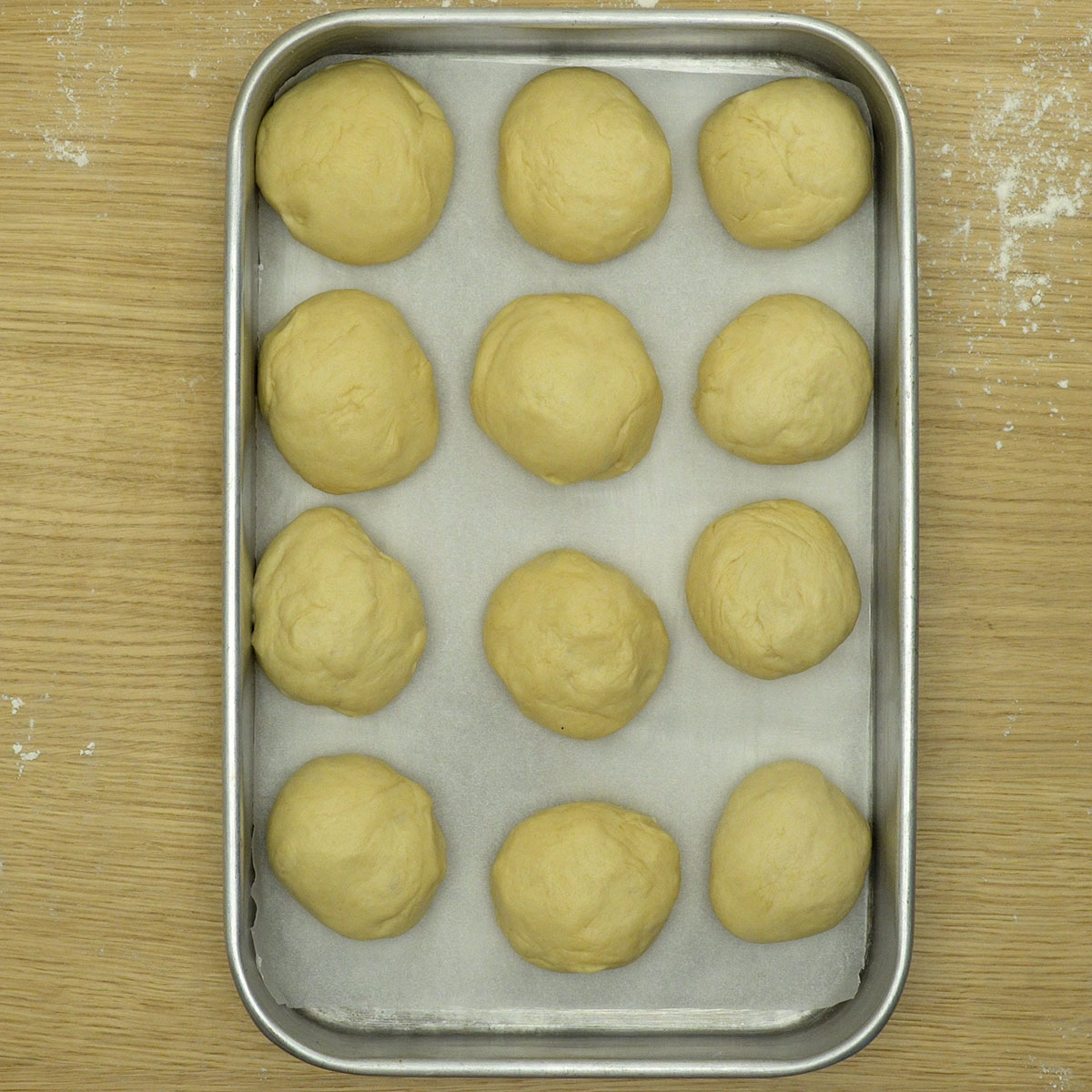Pães de cebola modelados e organizados em assadeira antes da fermentação.