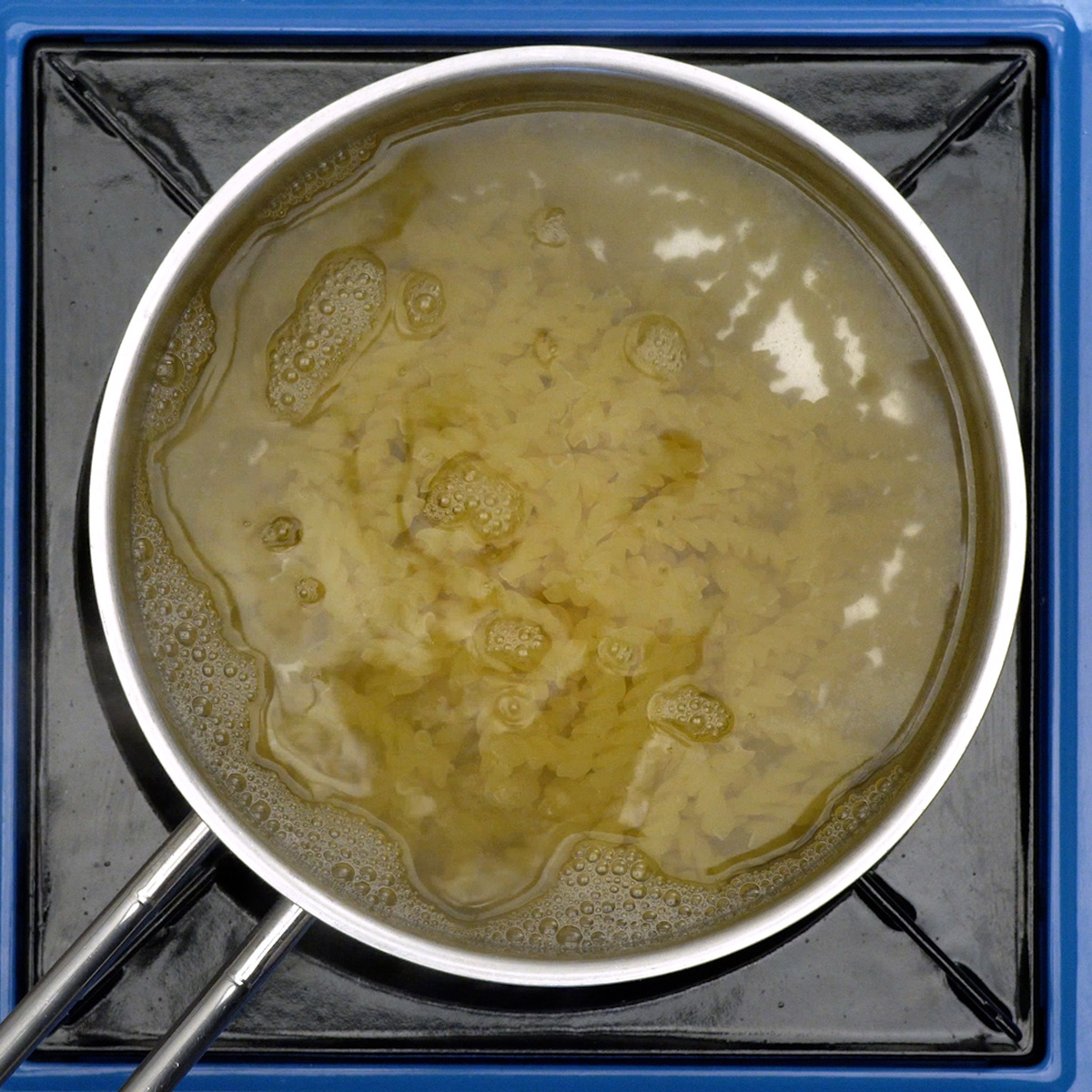 Macarrão espiral cozinhando em panela com água fervente e sal.