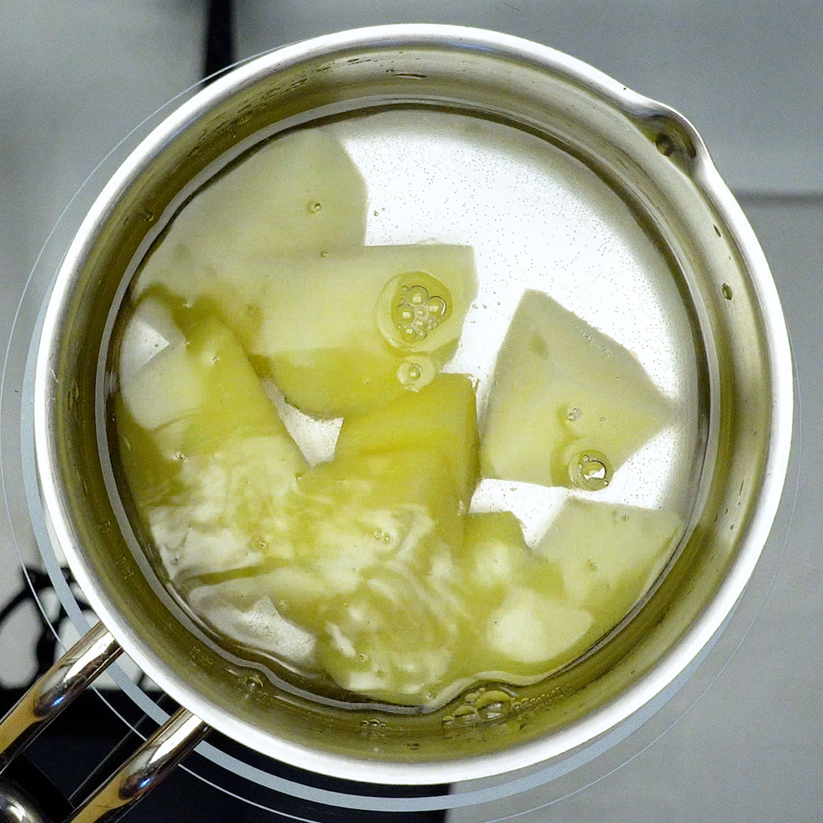 Batatas em pedaços cozinhando em panela com água até ficarem macias.