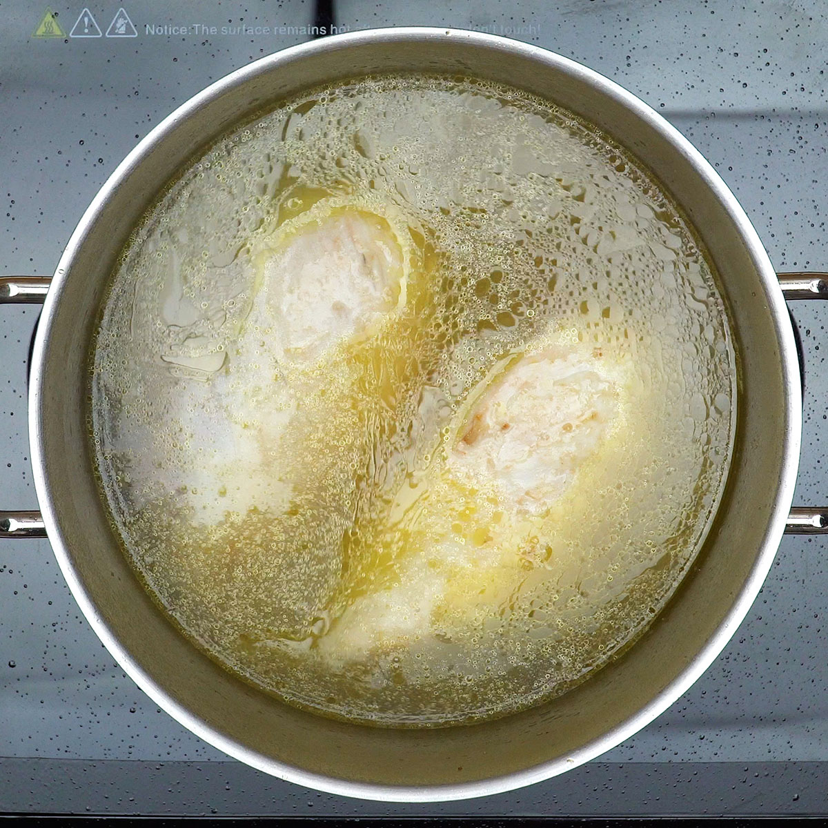 Frango cozinhando na panela com caldo e temperos para tortinhas salgadas.