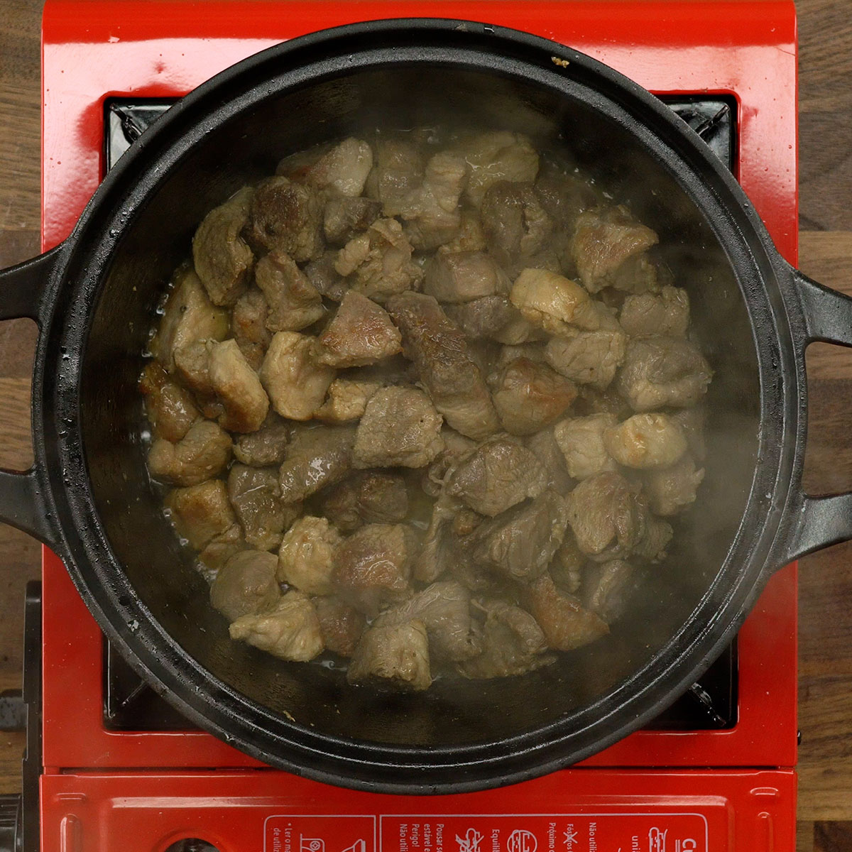 Carne de porco dourando em panela com azeite colocando um pouco de água quente.