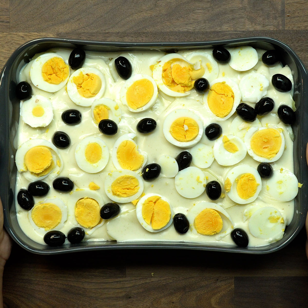 Bacalhau com molho branco decorado com ovos e azeitonas antes de ir ao forno.