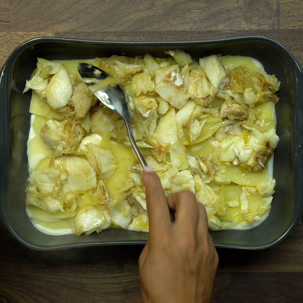 Camadas de batata, bacalhau e molho branco sendo montadas em refratário.