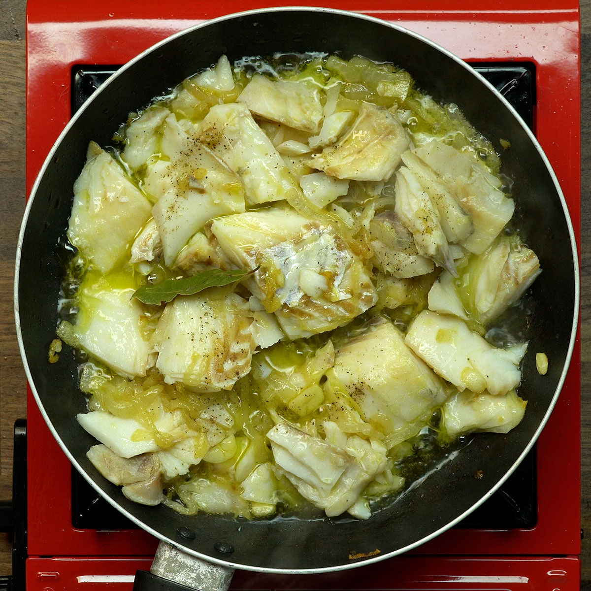 Bacalhau refogado com cebola e alho em frigideira.