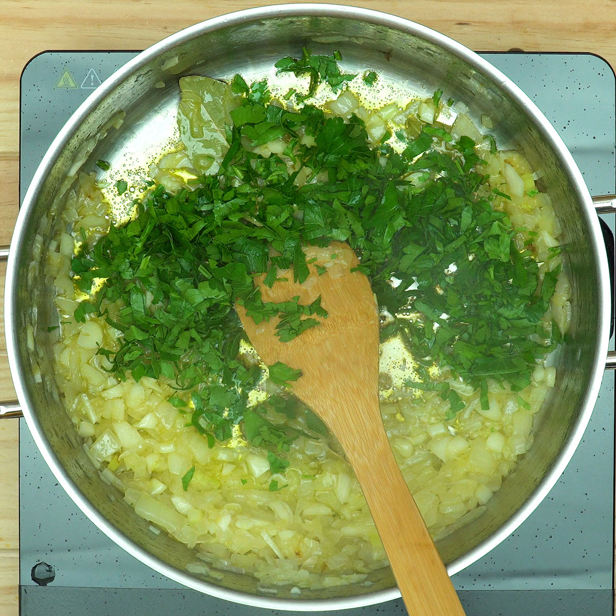 Louro e salsa sendo adicionados ao refogado para bacalhau com natas.