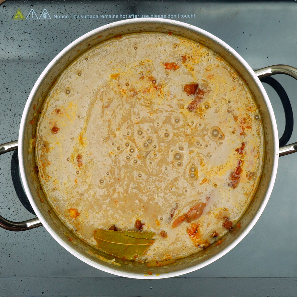 Caldo de feijão sendo adicionado à panela com os ingredientes refogados.