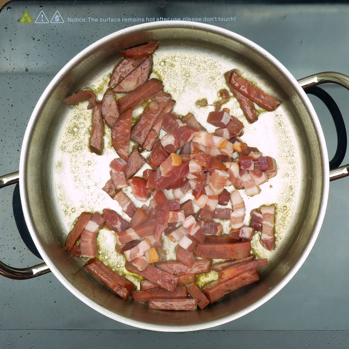 Calabresa e bacon dourando em panela até ficarem levemente crocantes.