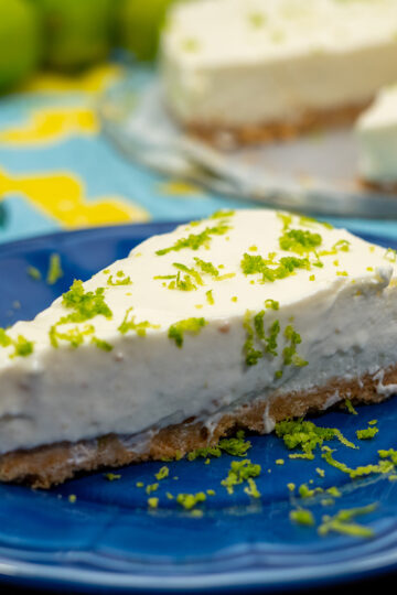 Fatia de cheesecake de limão finalizado com raspas de limão servido no prato.