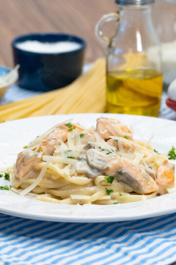 Empratamento linguine com salmão e cogumelo finalizado com queijo parmesão ralado.