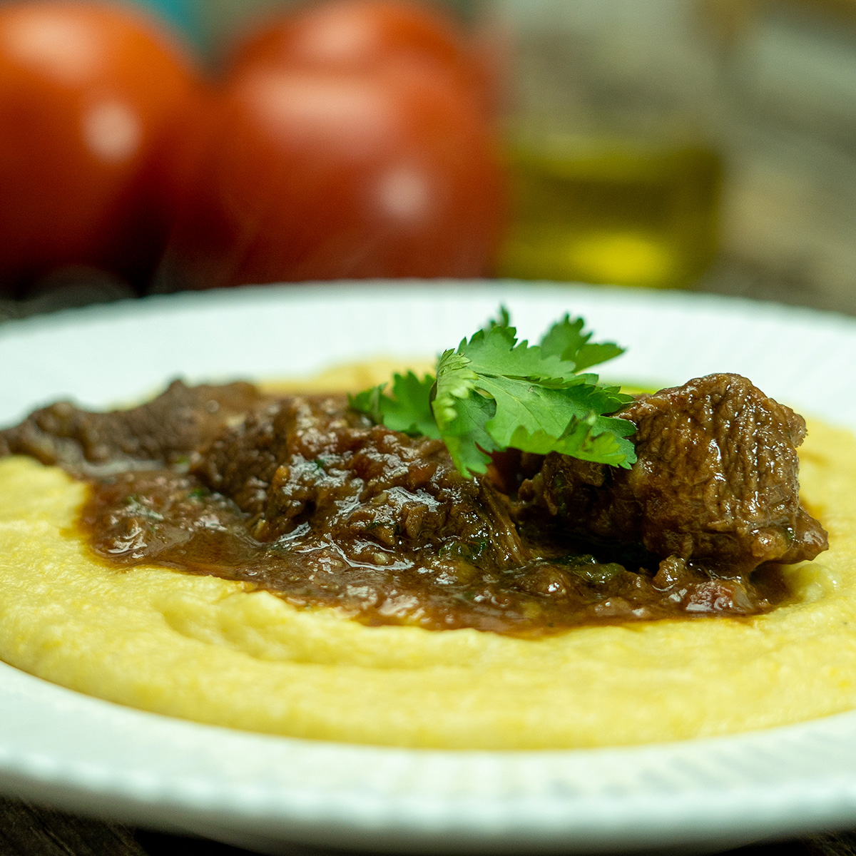 Empratamento ragu de carne com polenta cremosa finalizada com salsa como decoração.