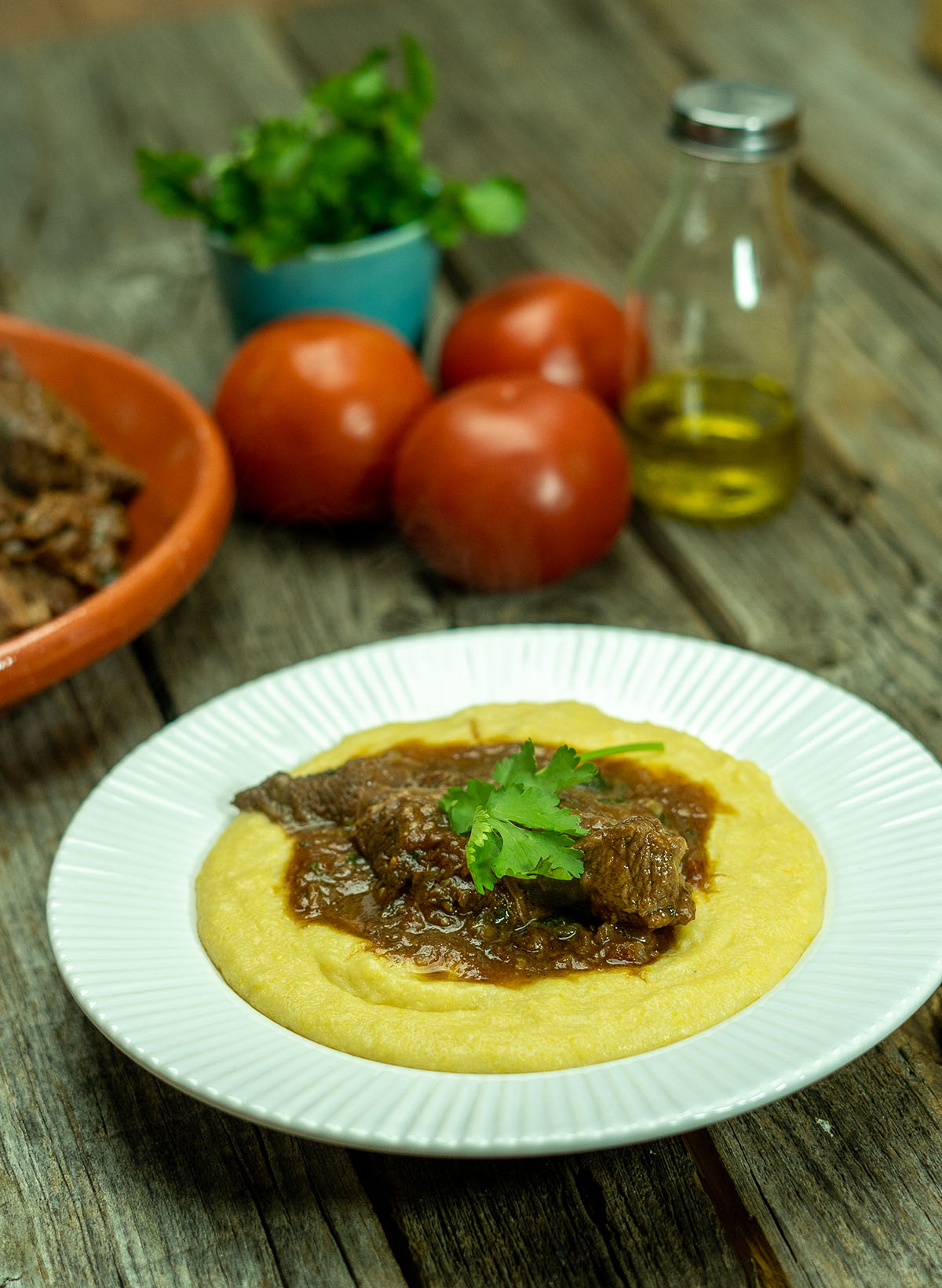Empratamento ragu de carne com polenta cremosa finalizada com salsa como decoração.