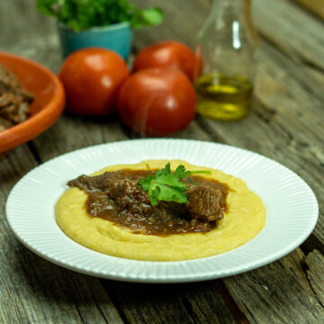 Empratamento ragu de carne com polenta cremosa finalizada com salsa como decoração.