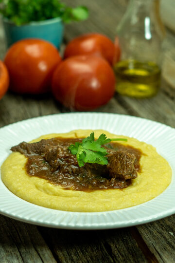 Empratamento ragu de carne com polenta cremosa finalizada com salsa como decoração.