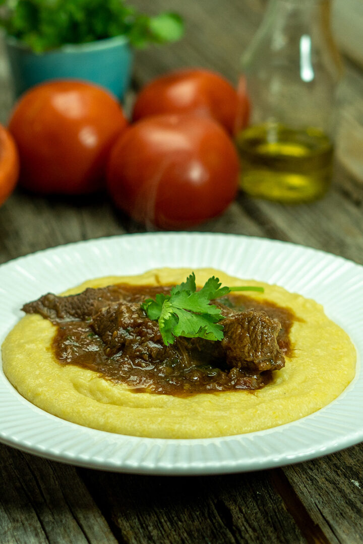 Empratamento ragu de carne com polenta cremosa finalizada com salsa como decoração.