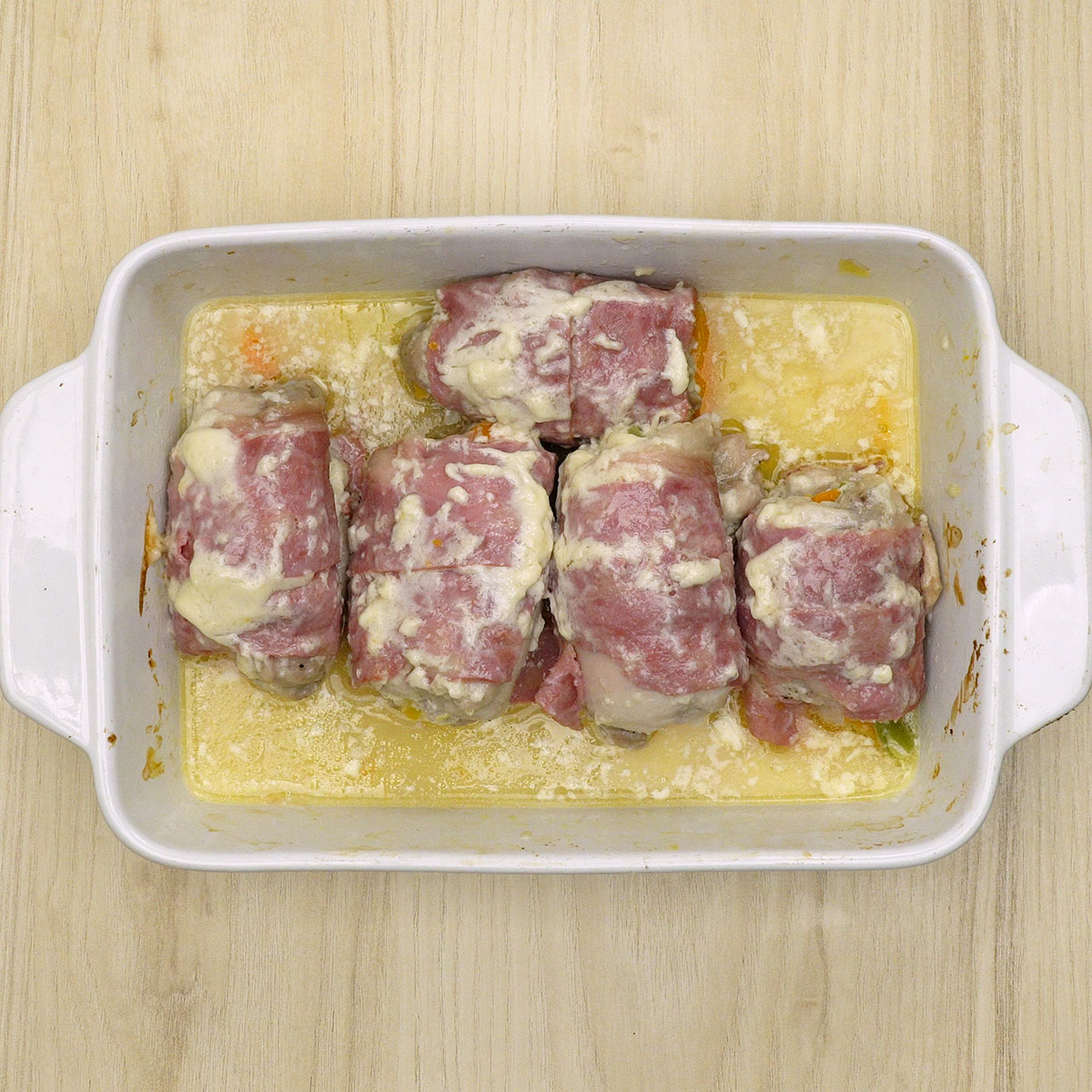 Enroladinhos de frango com bacon dourando no forno sem os legumes.