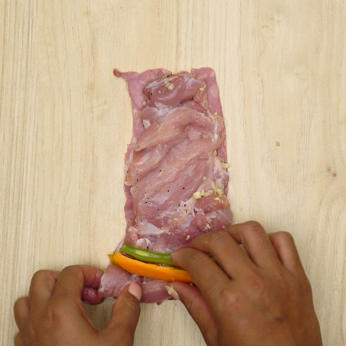 Filé de frango com tiras de pimentão, cenoura e vagem sendo enrolado com bacon e preso com palito.