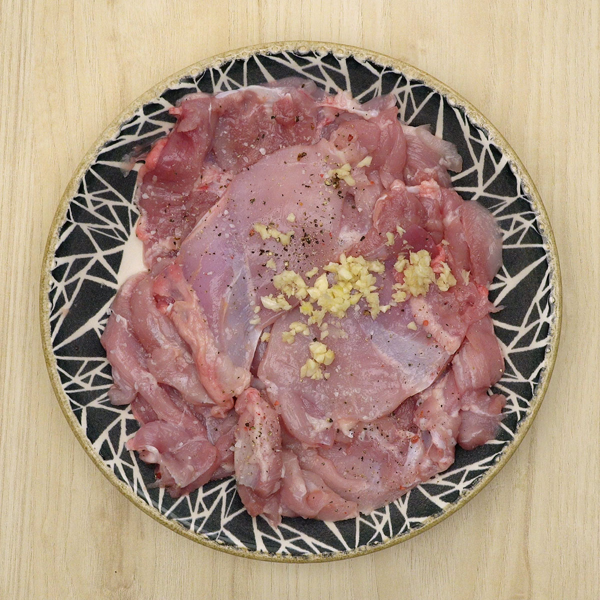 Sobrecoxa de frango aberta em manta sendo temperada com sal, pimenta e alho.