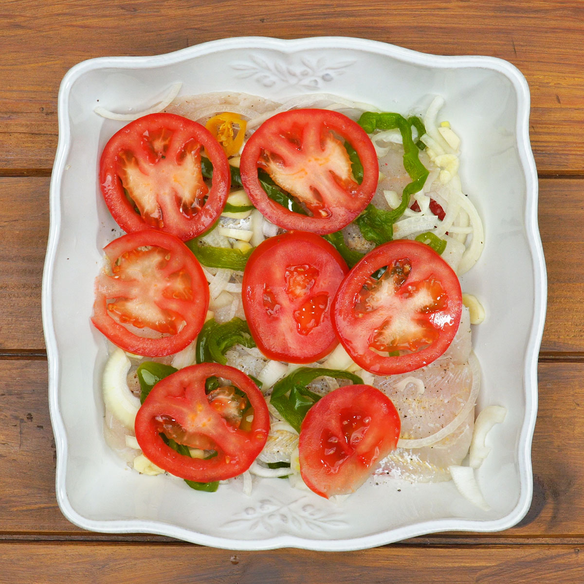 Filetes cobertos com tomate, alho e pimentão antes de assar.