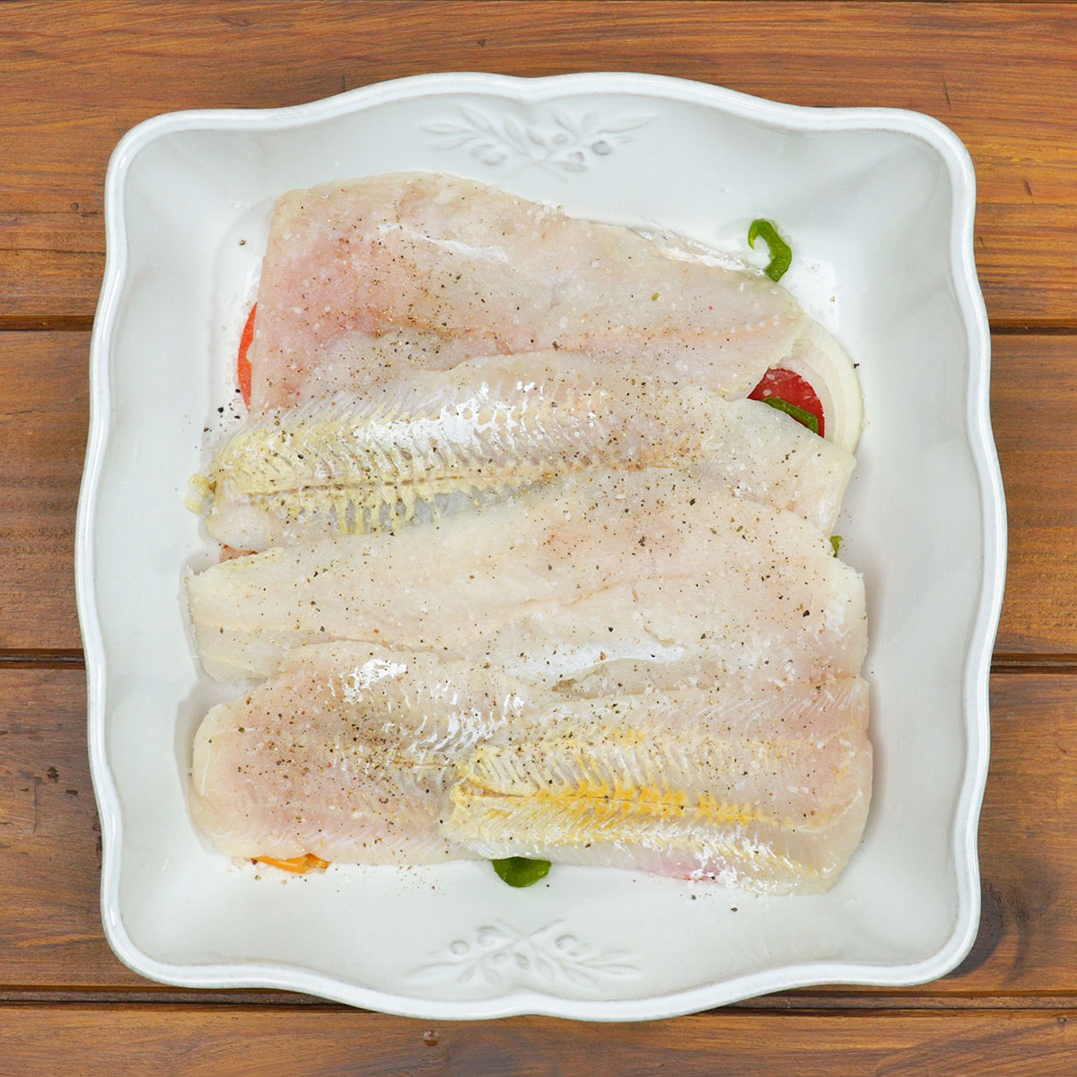 Filetes de peixe temperados sobre a camada de legumes na travessa.