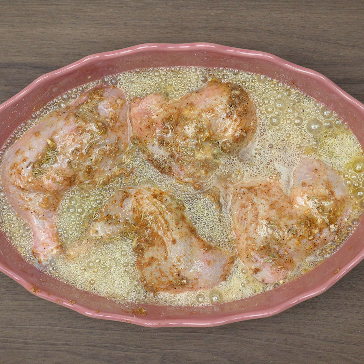Frango temperado com alecrim recebendo cerveja na travessa.