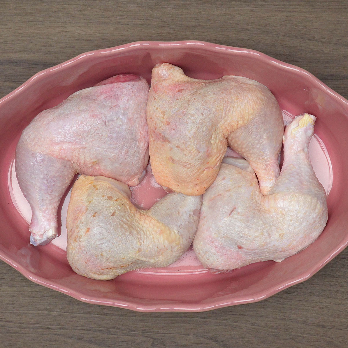 Pernas e sobrecoxas de frango organizadas em travessa refratária para assar.
