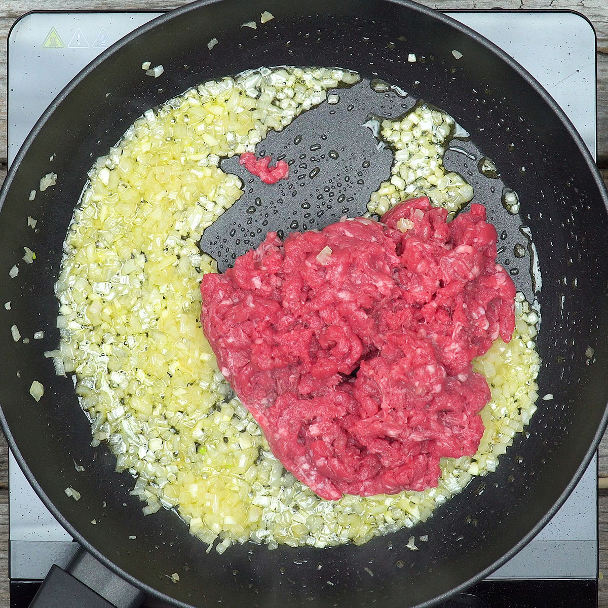 Carne moída dourando na frigideira e depois temperando com sal e pimenta.
