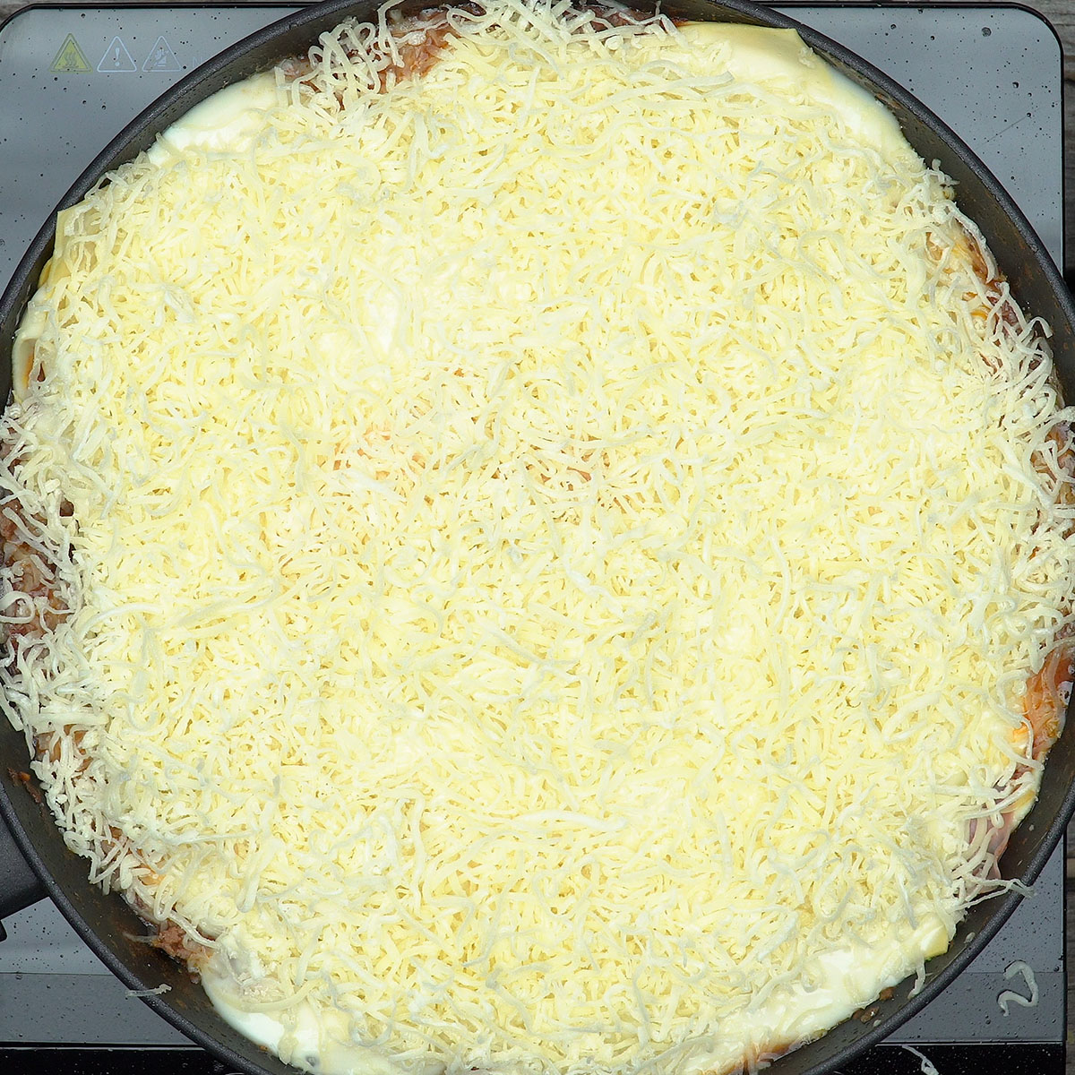 Massa para lasanha coberta com Catupiry e queijo ralado na frigideira.