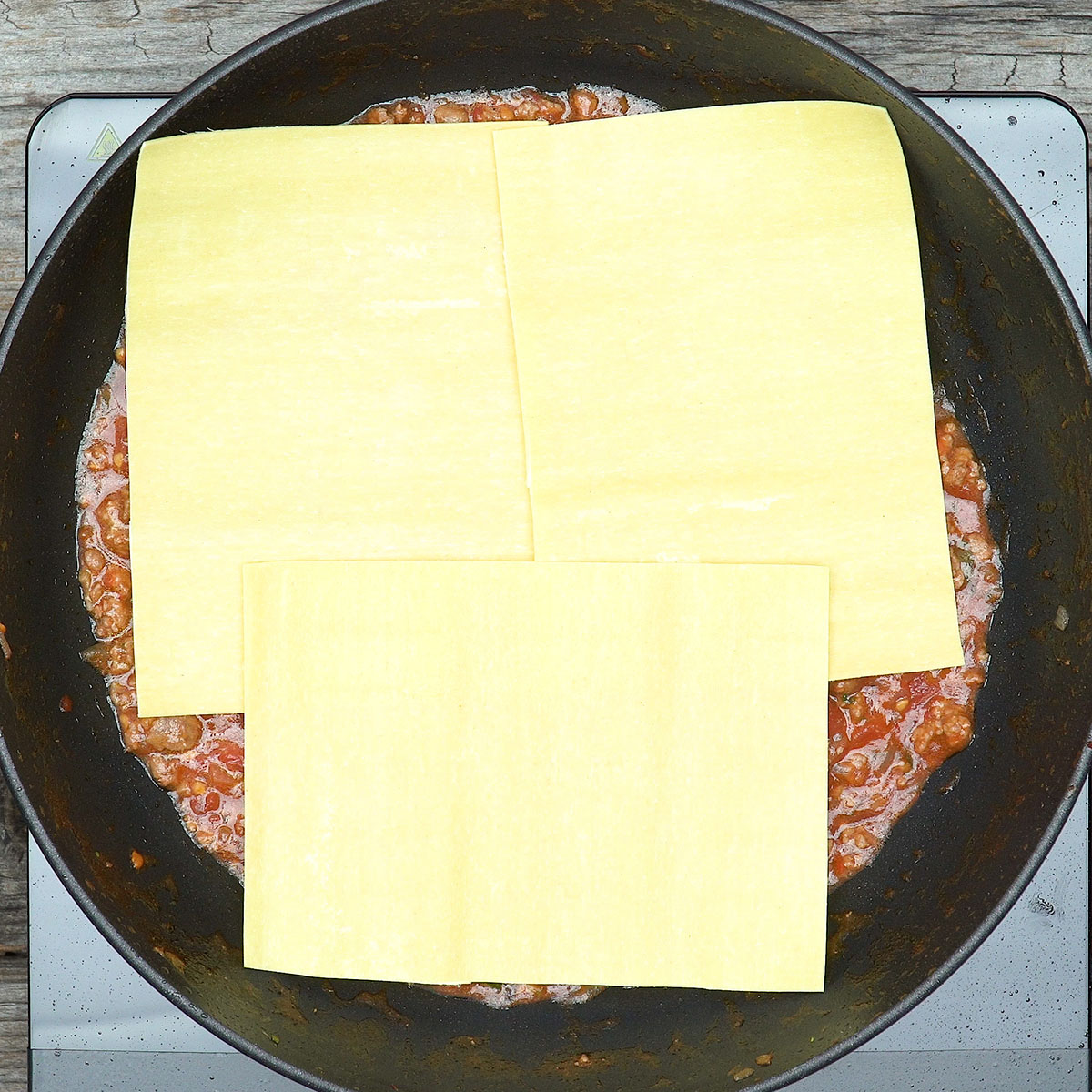 Montagem da lasanha de frigideira com molho de carne e folhas de massa.