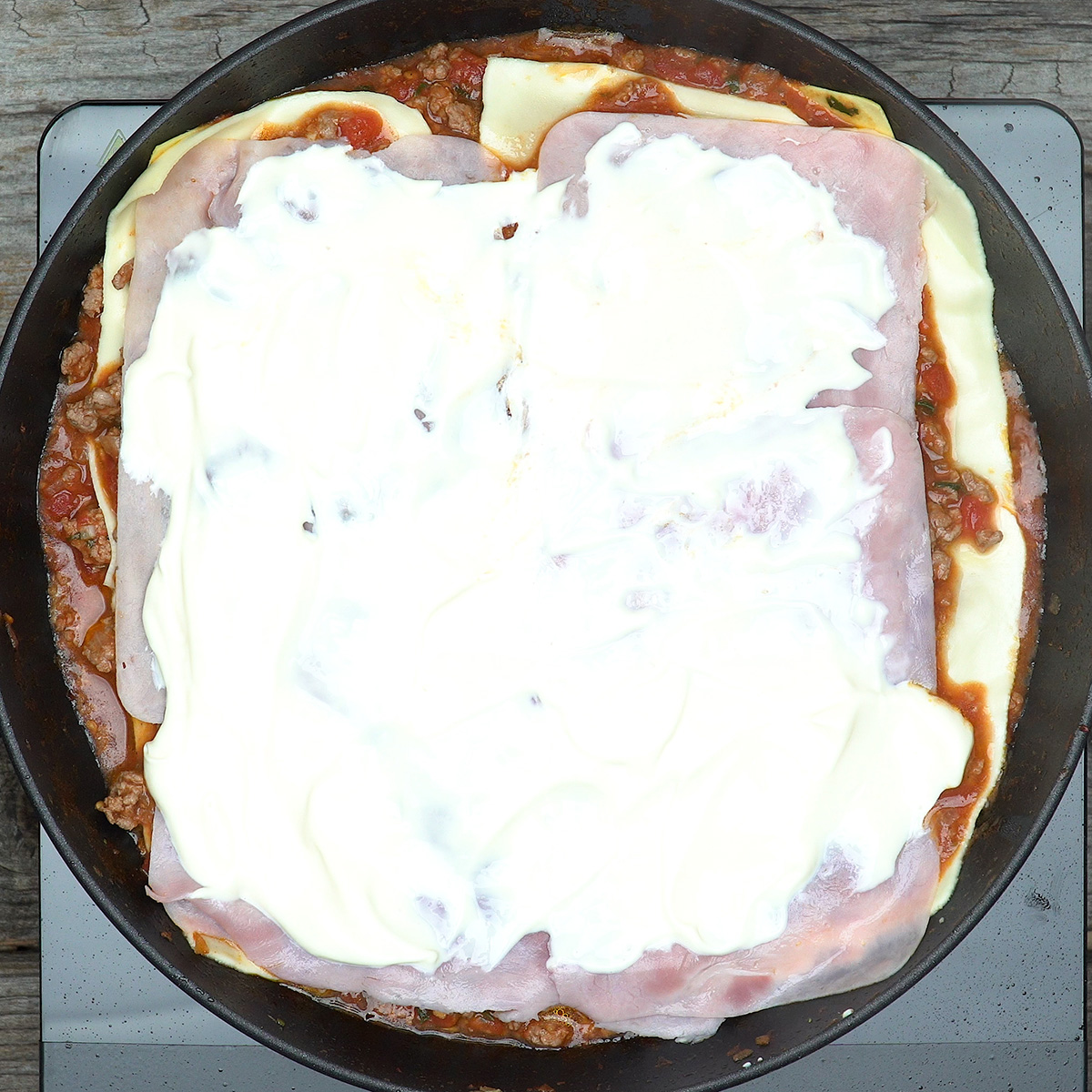Montagem das camadas de lasanha de frigideira com molho, queijo, fiambre e Catupiry.