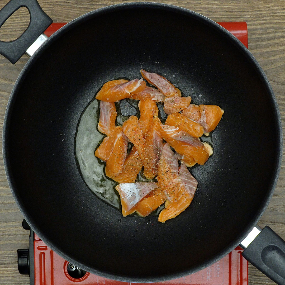 Cubos de salmão dourando em frigideira com azeite.