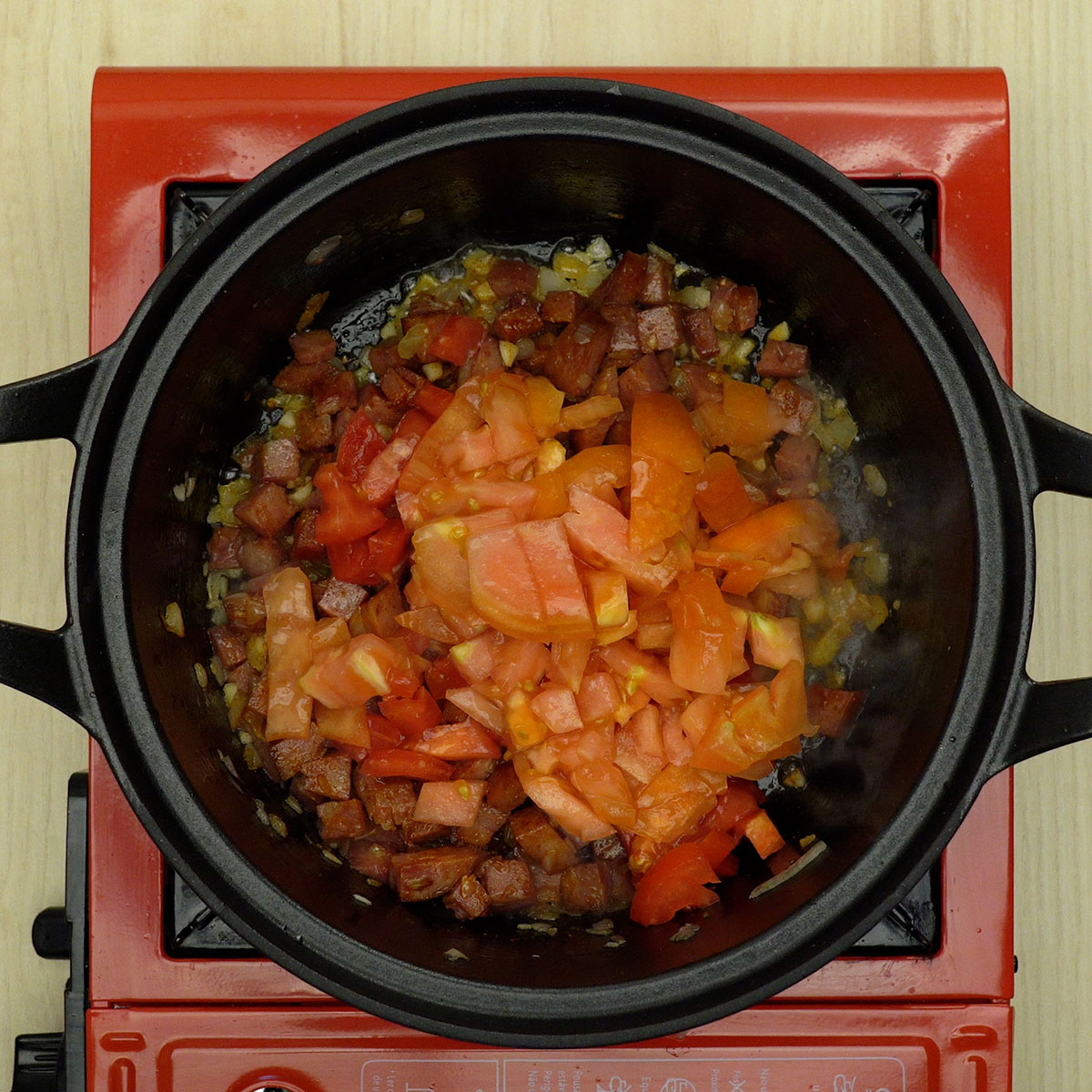Tomate fresco sendo incorporado ao refogado de calabresa e temperos.