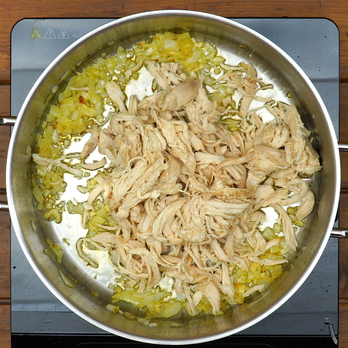 Frango desfiado sendo refogado para macarrão gratinado com frango.