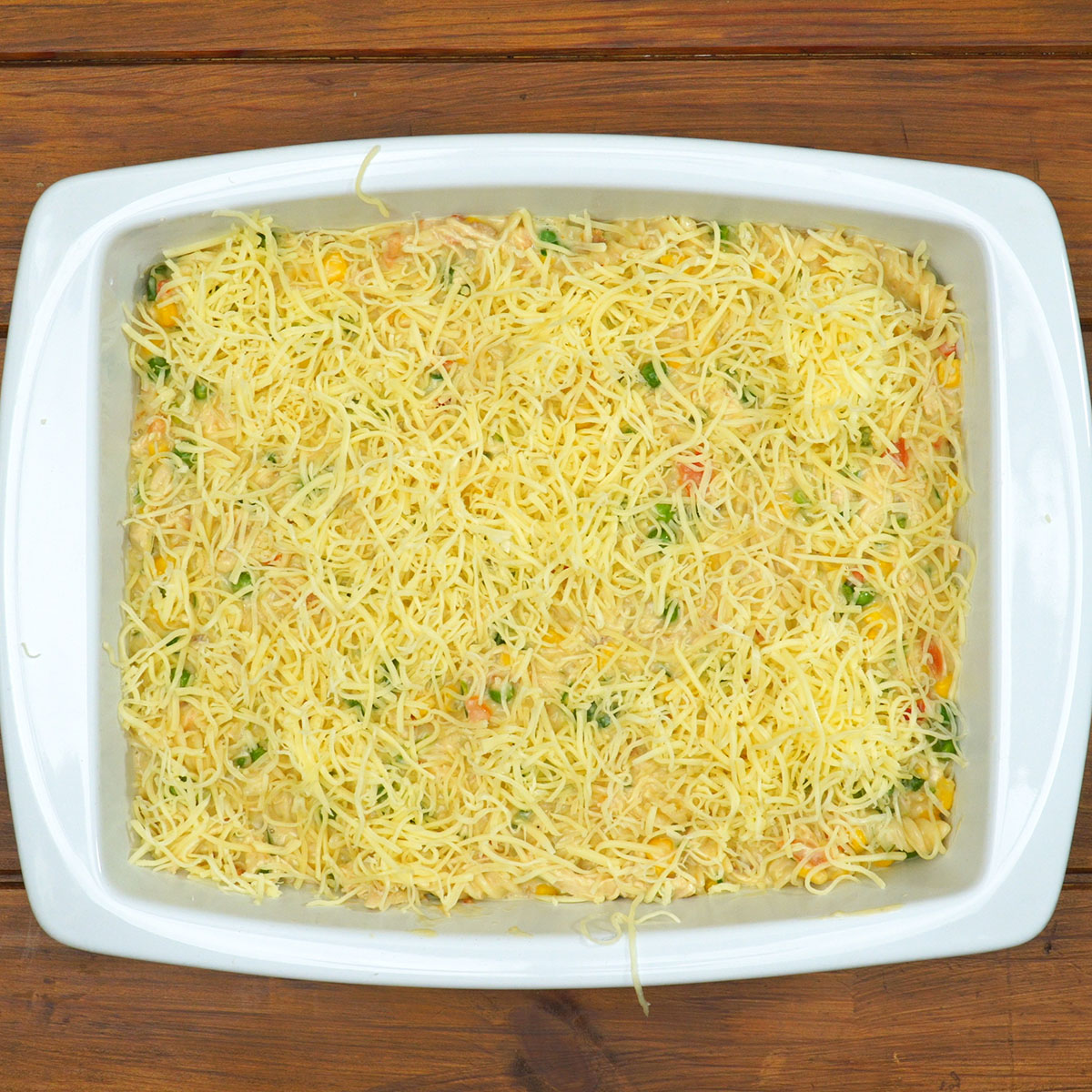 Macarrão gratinado com frango coberto com queijo antes de assar.