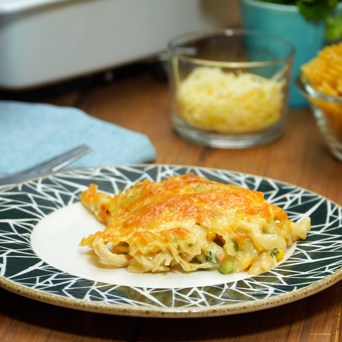 Macarrão gratinado com frango servido quente e finalizado com coentros.