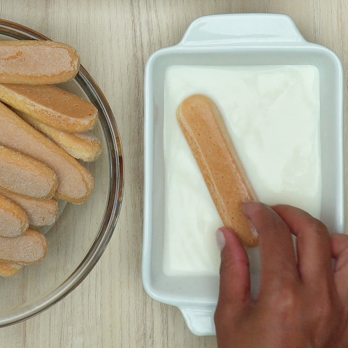 Biscoitos champagne sendo umedecidos em leite para a montagem do pavê.