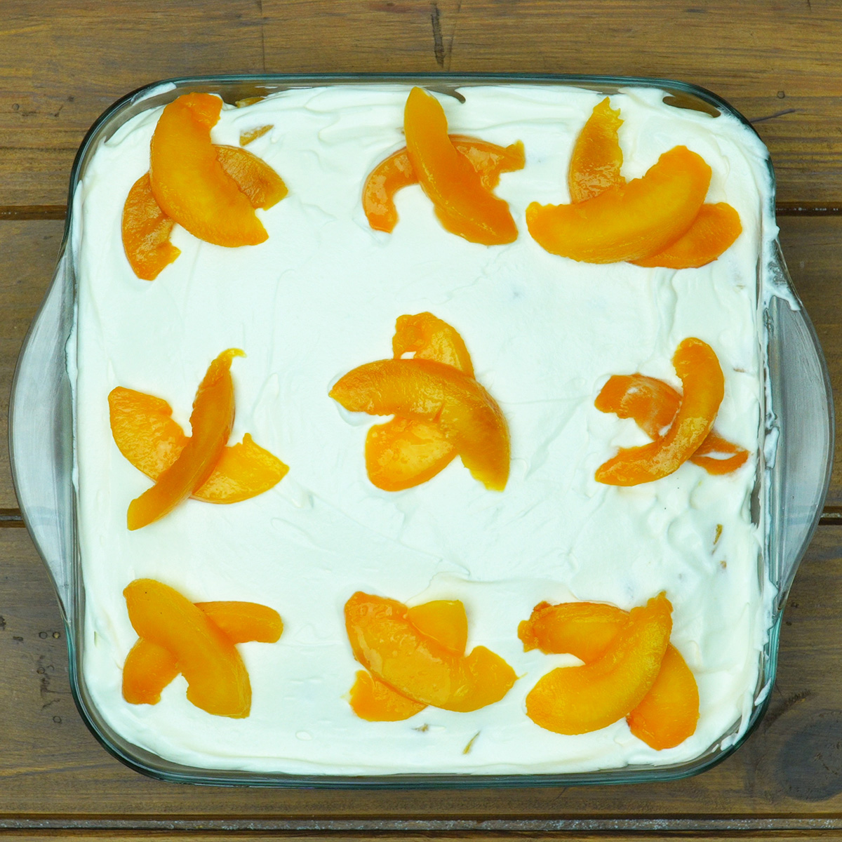 Pavê de pêssego coberto com chantilly e decorado com frutas.