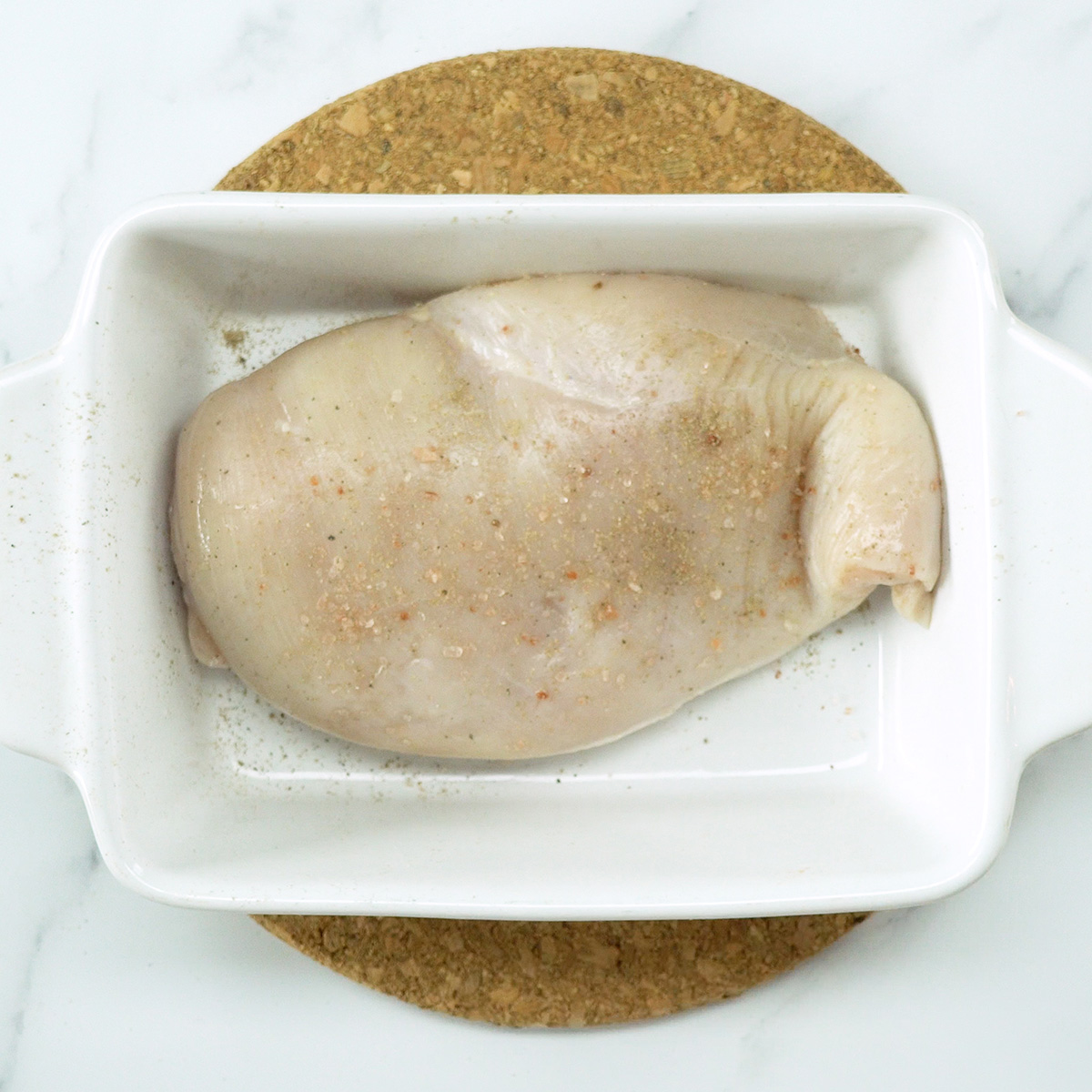 Peito de frango sendo temperado com sal antes do forno.