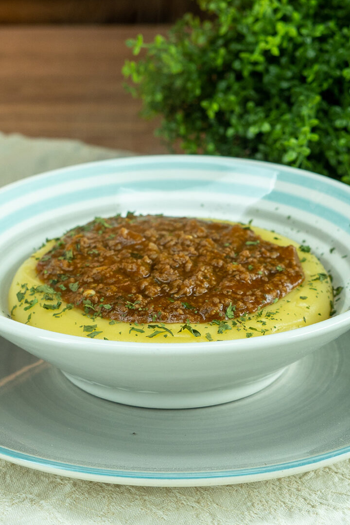 Empratamento polenta cremosa servida com molho de carne moída finalizado com salsinha.