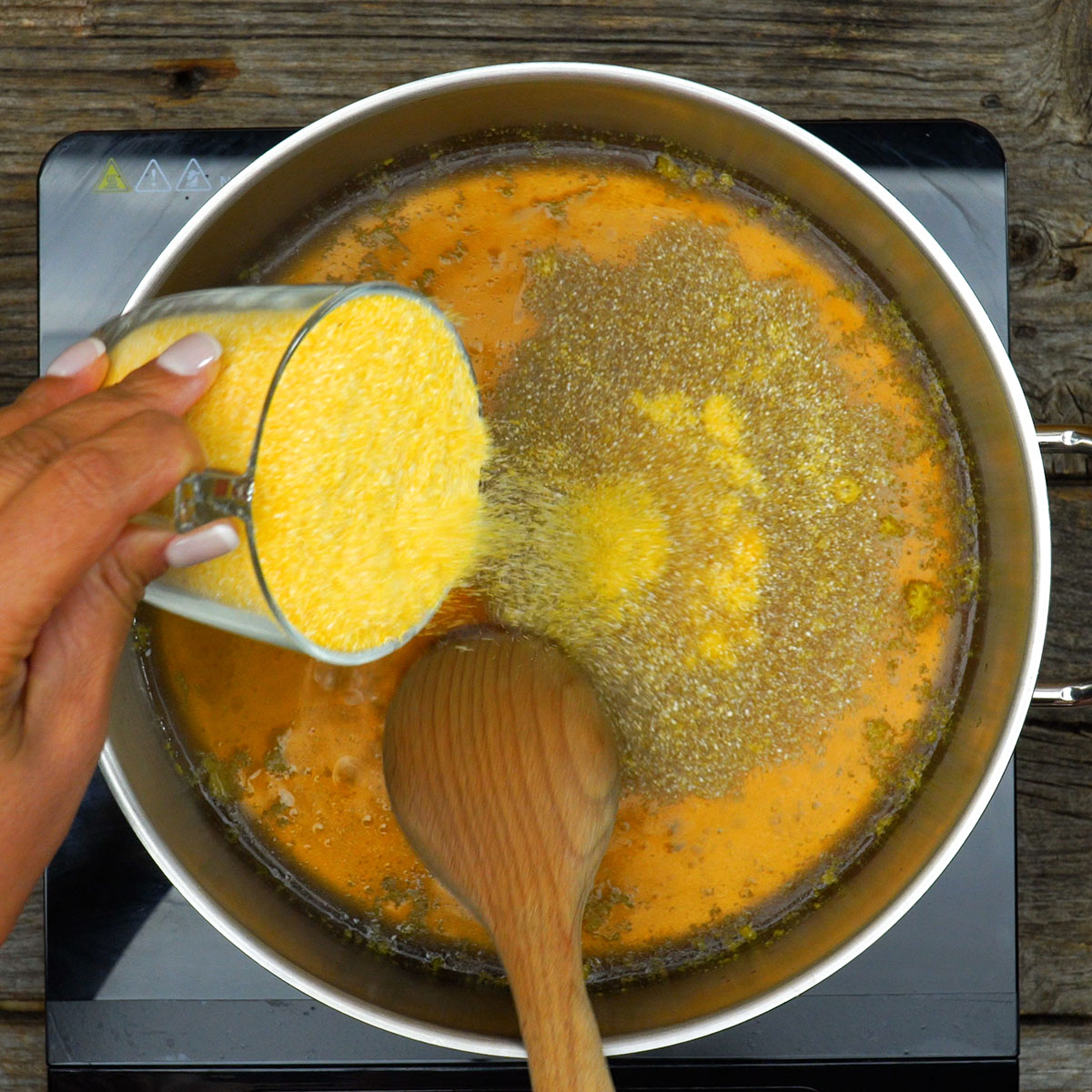 Farinha de milho sendo misturada ao caldo de legumes para preparar polenta cremosa.