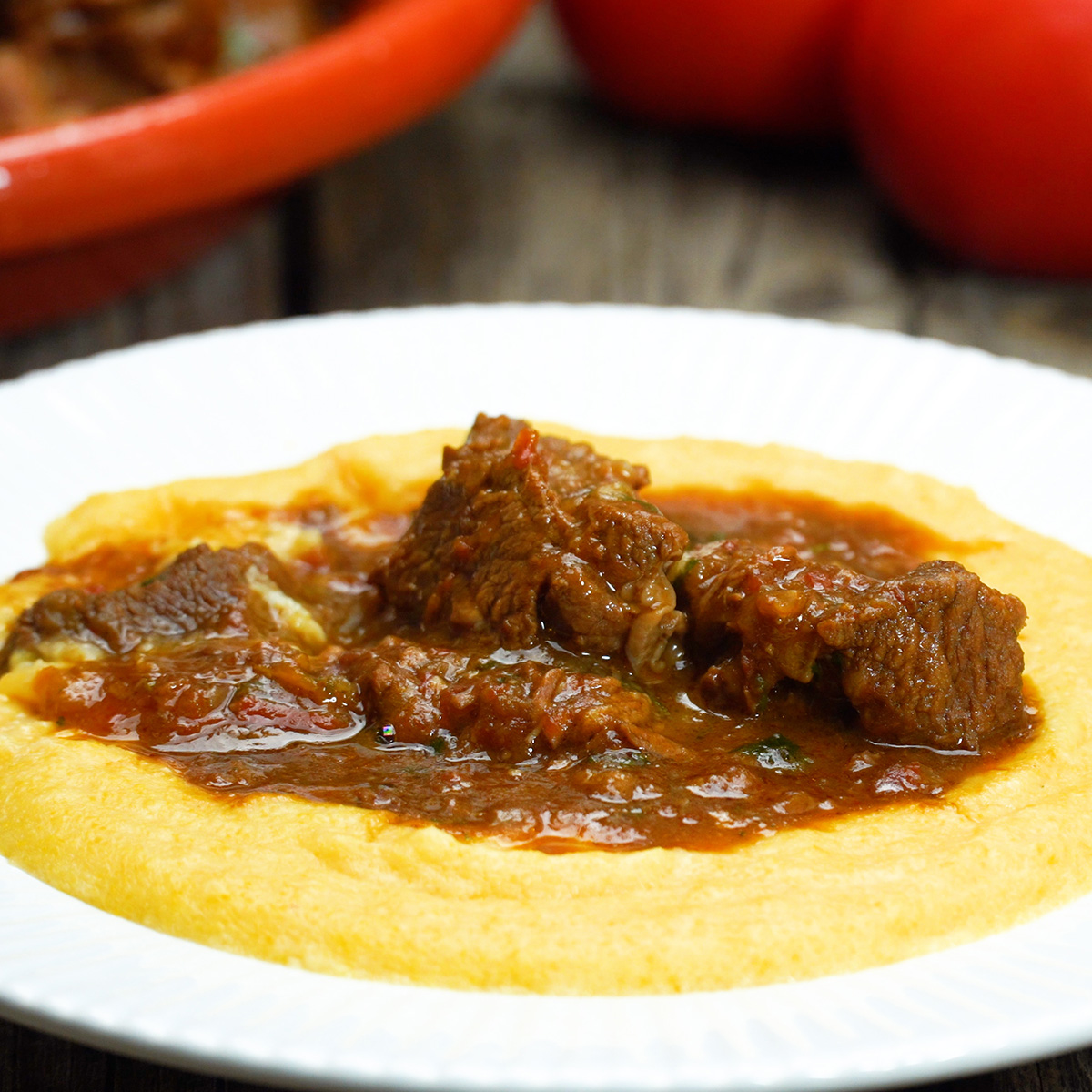 Ragu de carne servido sobre polenta cremosa em prato fundo.