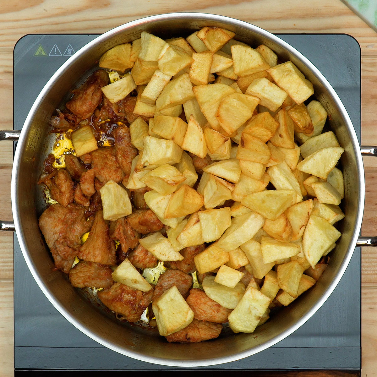 Batatas fritas misturadas com a carne dourada na frigideira.